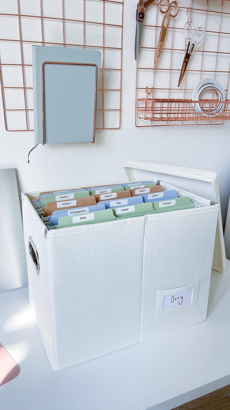 White fabric storage bin filled with labeled colored hanging file folders on a desk.