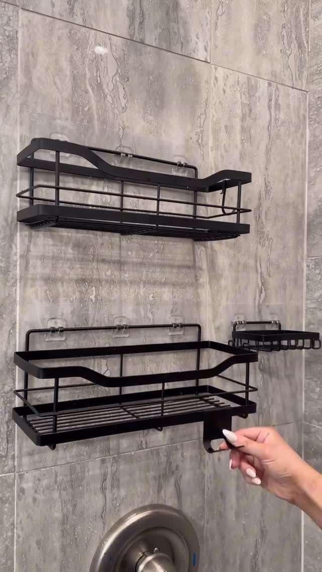 Black metal shower caddies mounted on a grey marbled tile bathroom wall.