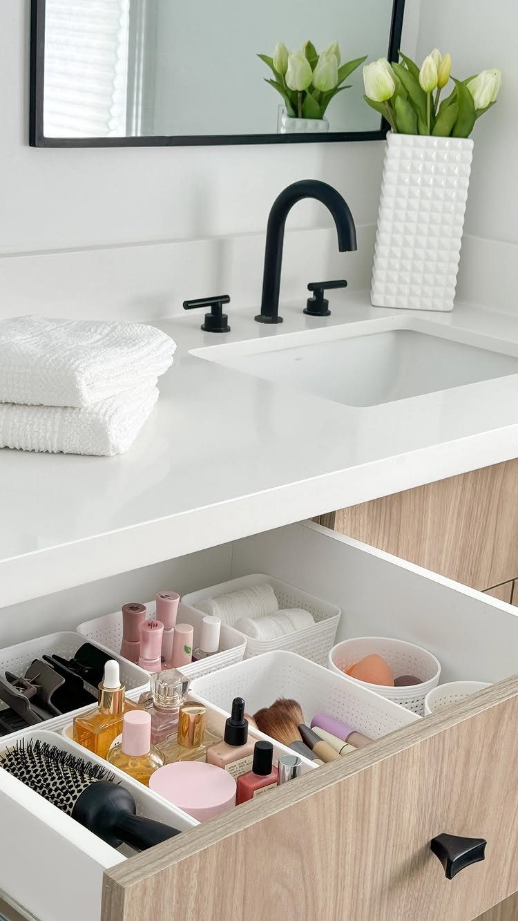 Open bathroom drawer with white organizers holding makeup, skincare, and beauty tools.