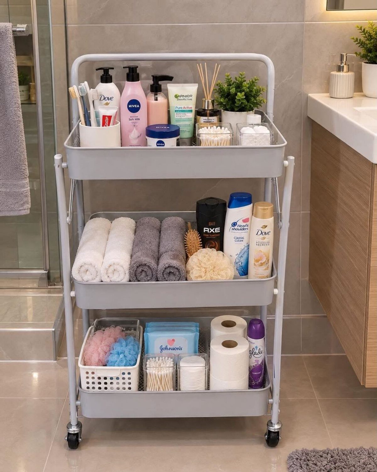 Grey three-tier rolling cart holding towels, toiletries, and baskets in a modern bathroom.