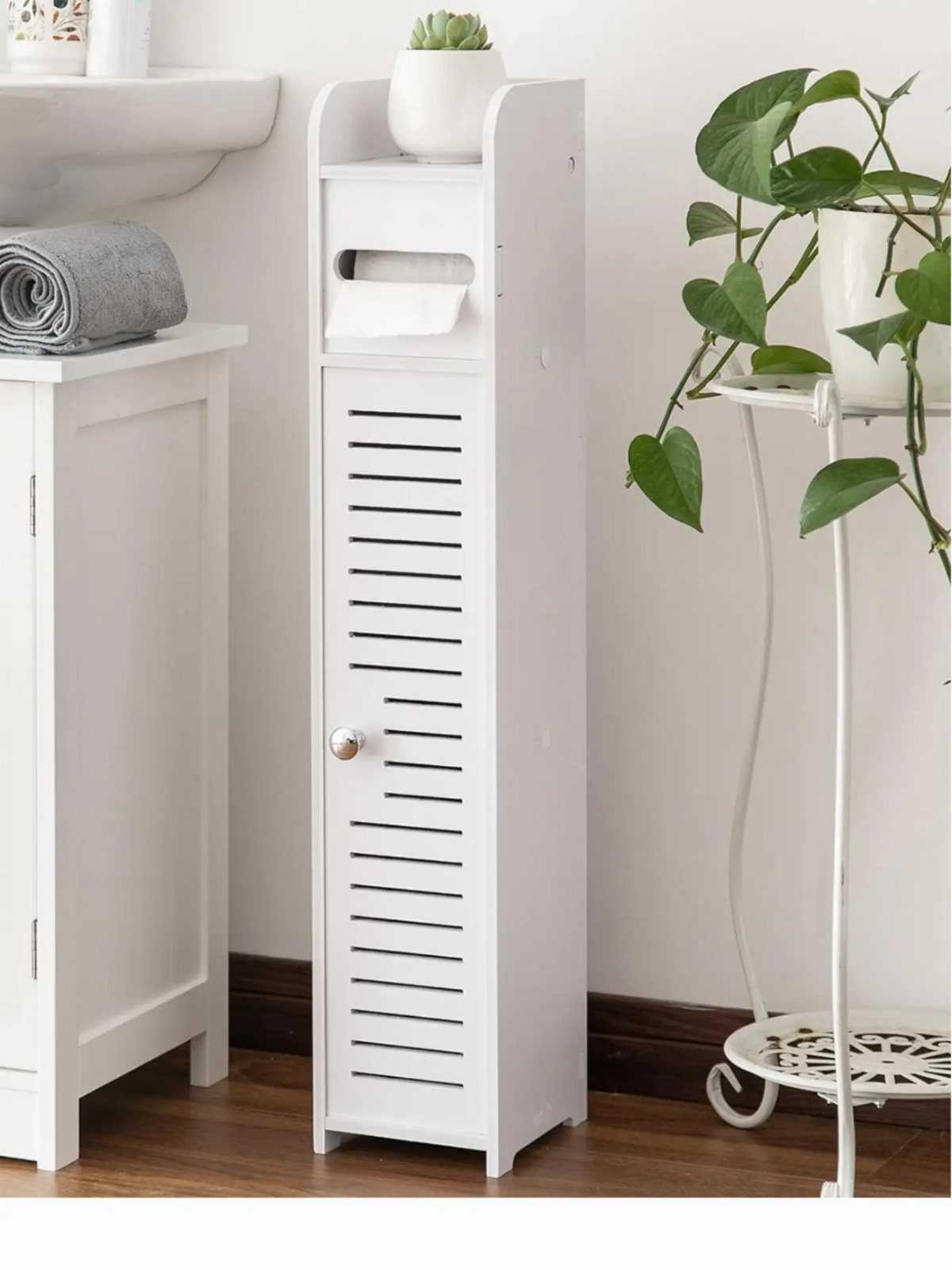 Slim white vertical storage cabinet with slatted door in a bright bathroom setting.