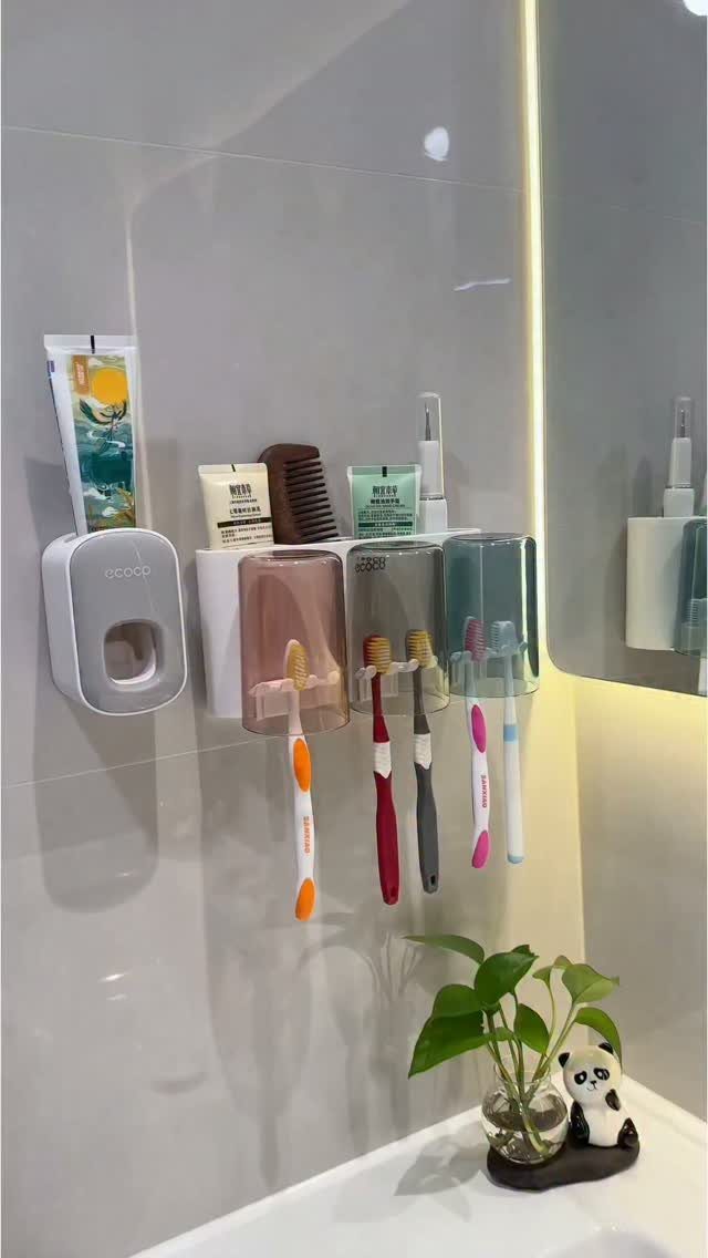 Wall-mounted toothbrush holder with colorful compartments holding toothbrushes and toothpaste on grey tiles.