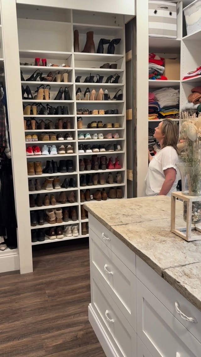 White walk-in closet with organized shoe shelves, folded clothes, and a marble island.