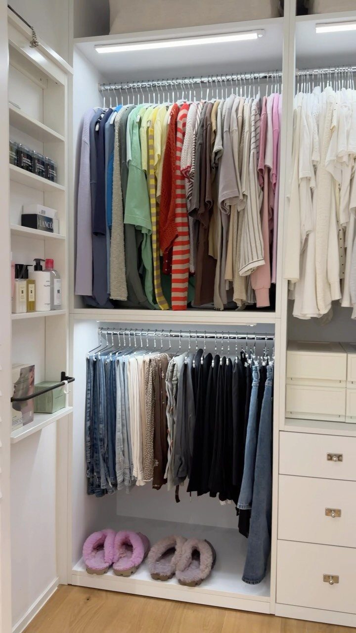 Clothing arranged in a rainbow color gradient on white closet hanging rods.