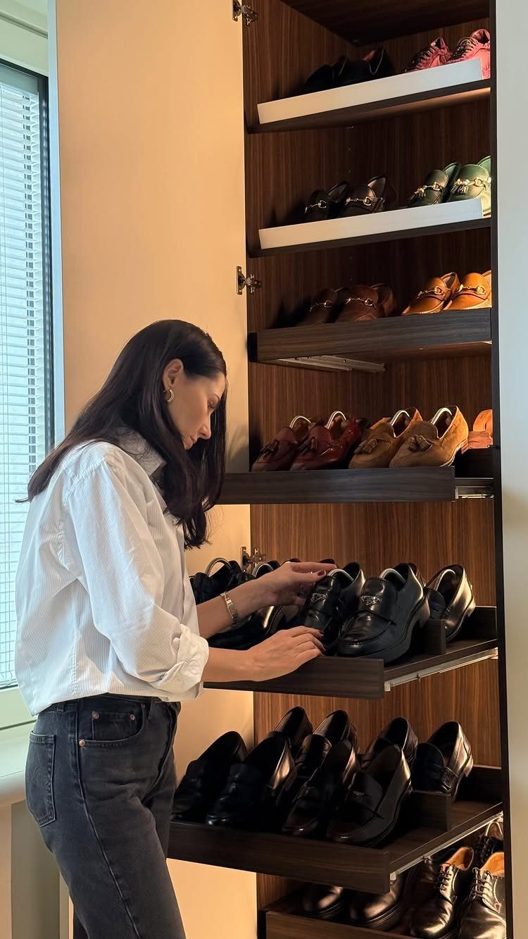Woman organizing a dark wood walk-in closet shelf filled with dress shoes.