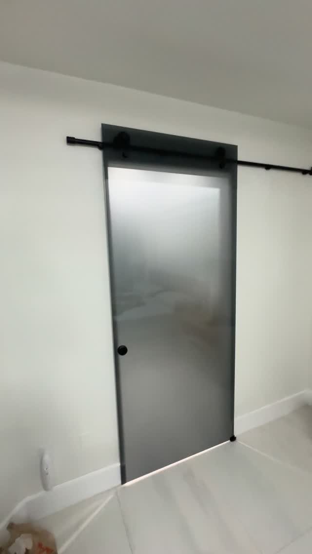 Frosted glass sliding barn door with black hardware on a white wall.