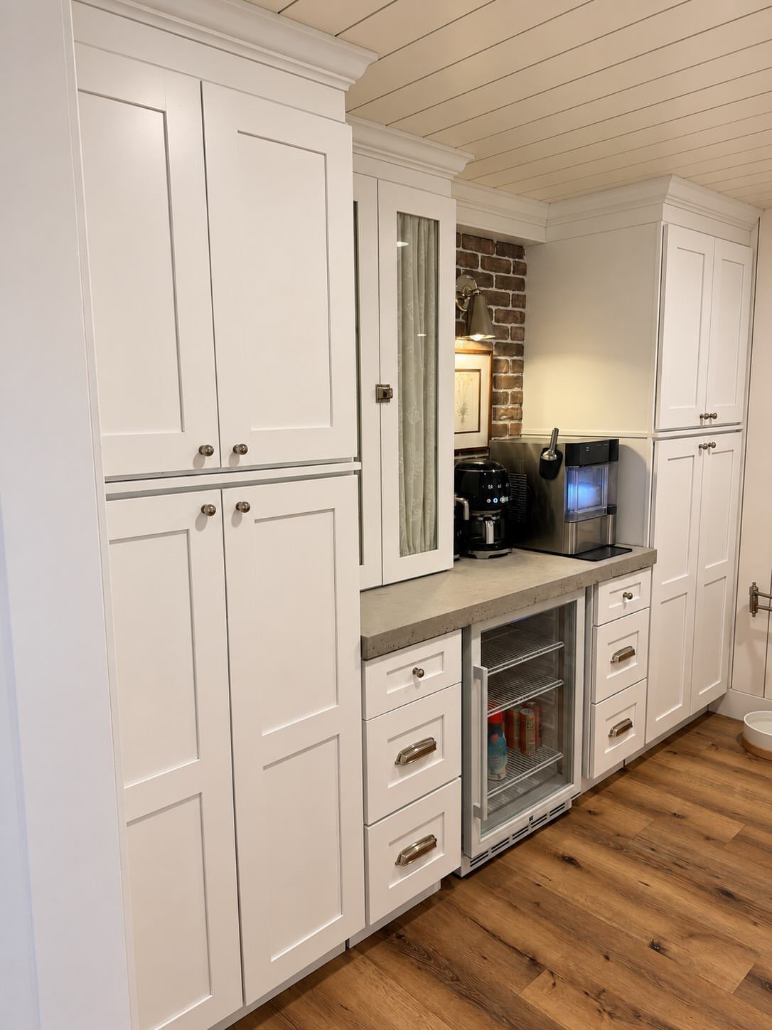 Beverage refrigerator integrated under a grey countertop with white cabinetry and wood flooring.