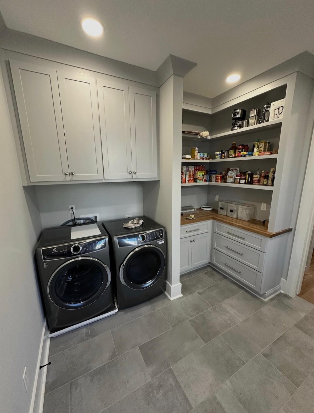 Laundry and pantry combo with grey cabinets, washer, dryer, and open food shelving.