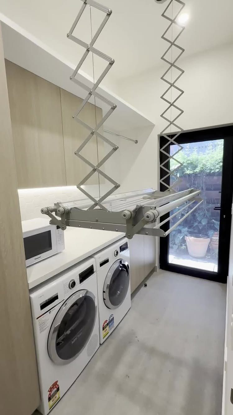 Laundry room with white washing machines, microwave, and a ceiling-mounted drying rack.