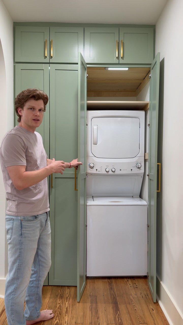 Man standing by sage green cabinets opening to reveal stacked white laundry machines.