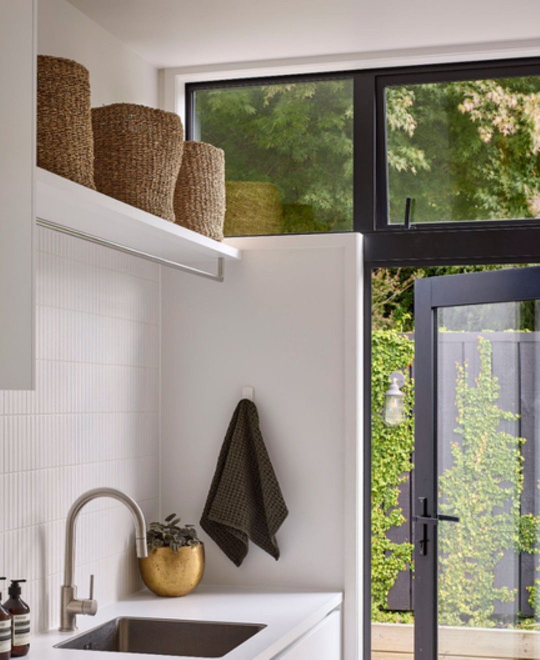 White utility room with stainless steel sink, woven baskets, and a glass door.