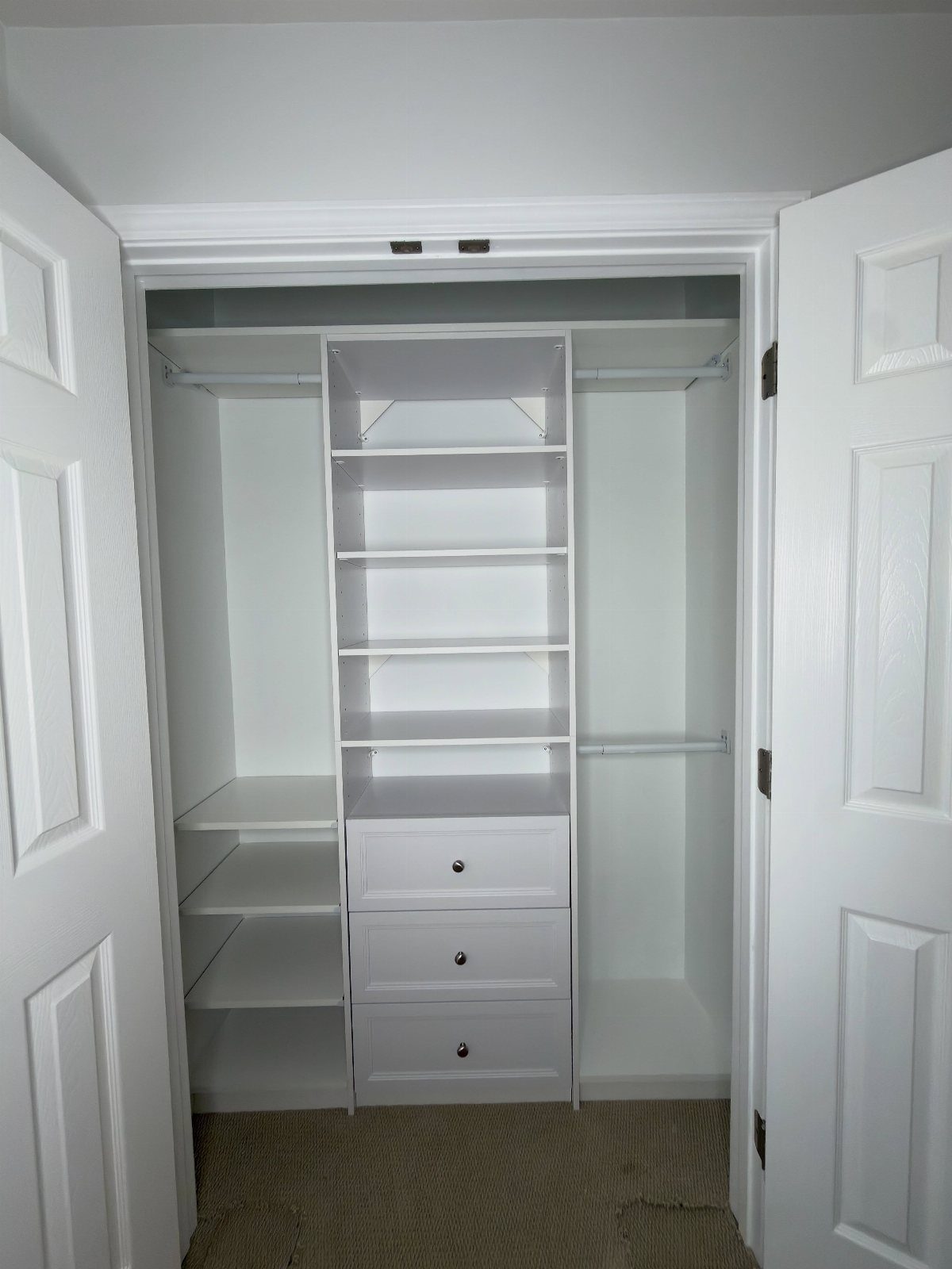 White reach-in closet with central shelving tower, drawers, and hanging rods.