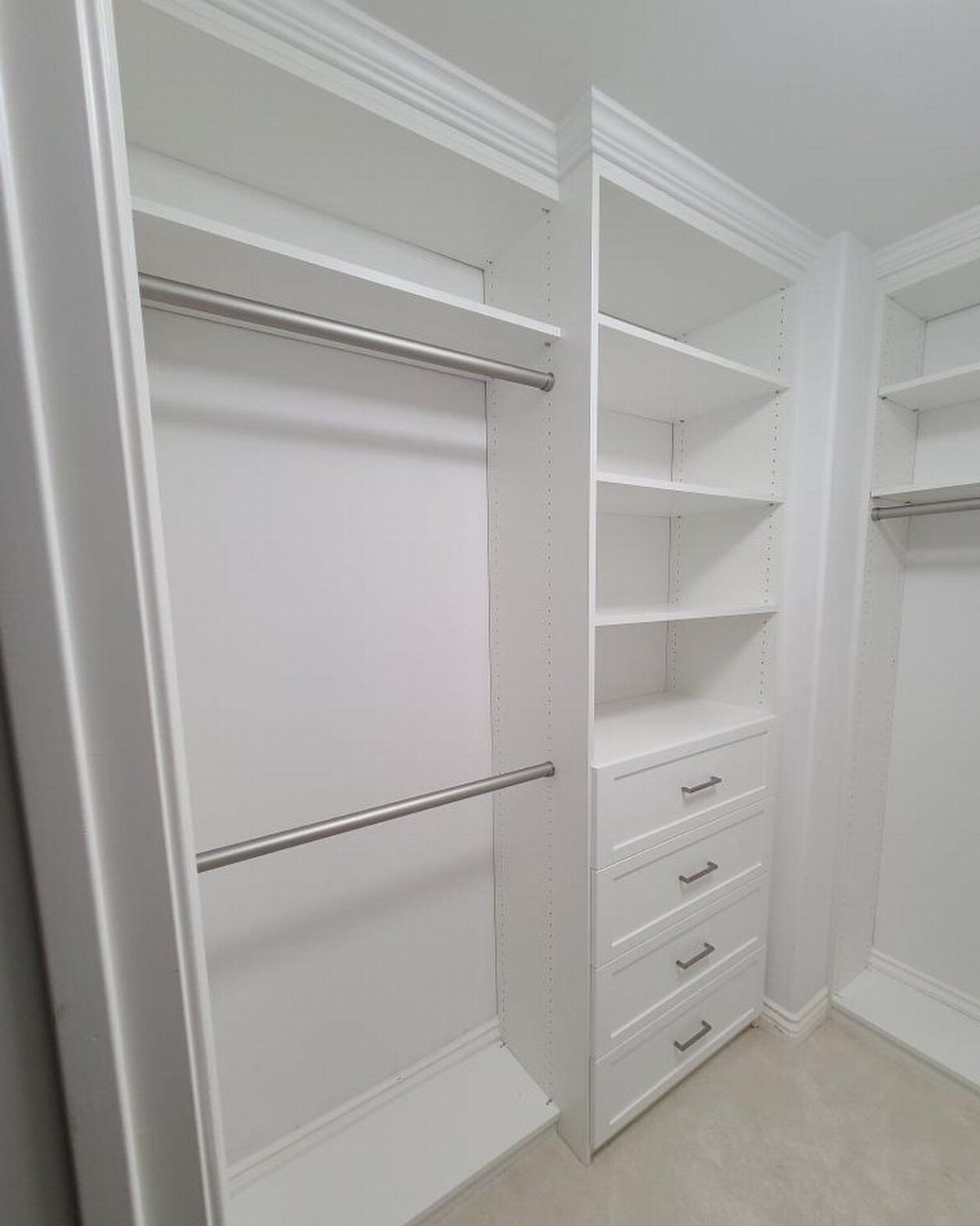 White closet interior with double hanging rods, drawers, and decorative crown molding top.