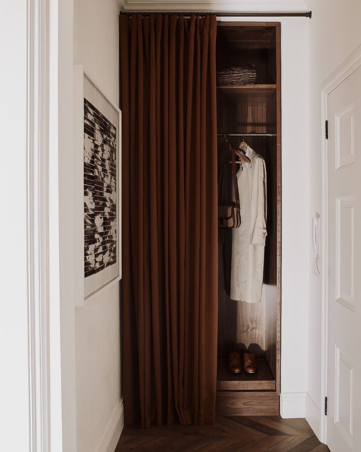 Brown curtain covering a wooden reach-in closet with a white dress hanging inside.