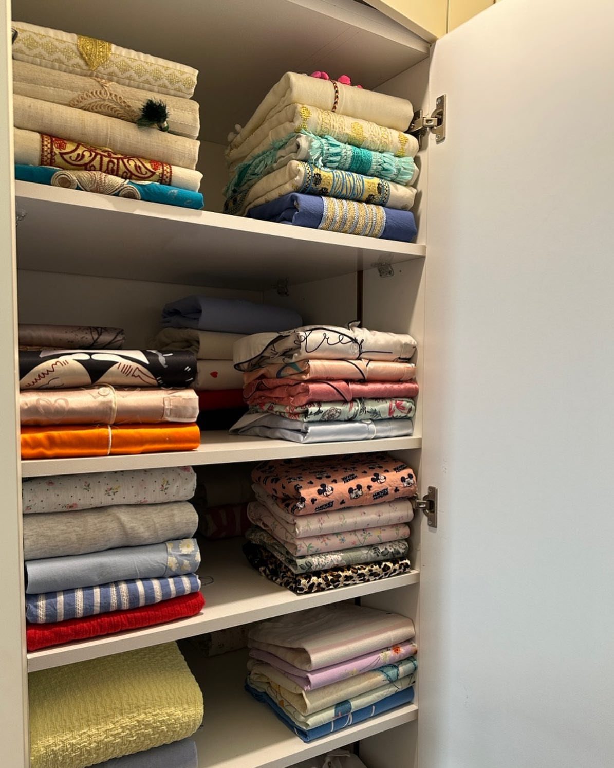 White closet shelves filled with neatly folded stacks of colorful patterned fabrics.