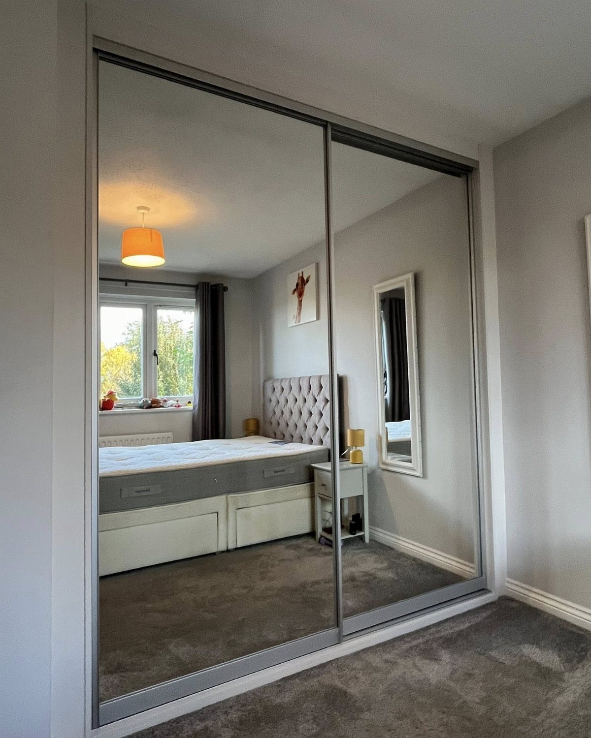 Mirrored sliding closet doors reflecting a modern bedroom with grey walls and carpet.