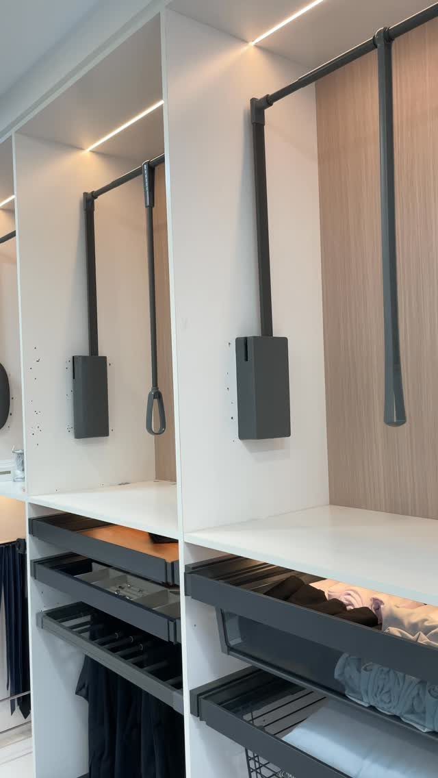 Pull-down clothing racks in a white modern closet with integrated LED lighting and drawers