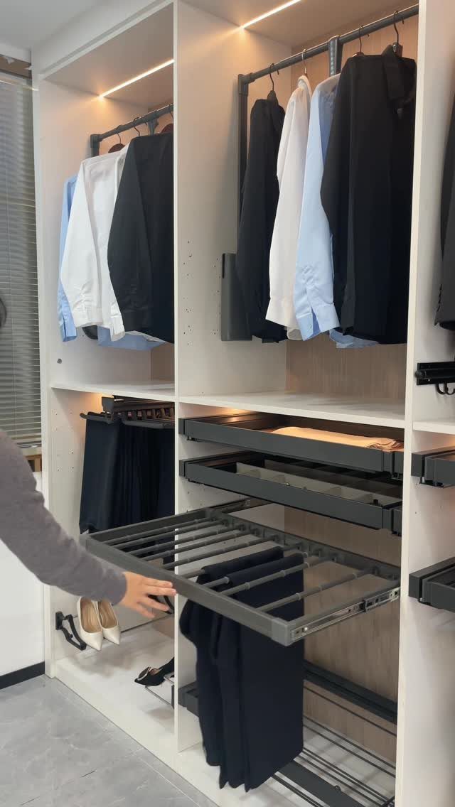 White reach-in closet with integrated lighting, hanging clothes, and pull-out trouser racks.