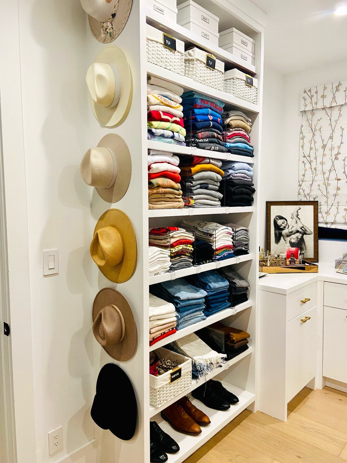 Hats hanging on wall hooks next to organized white closet shelving and drawers.