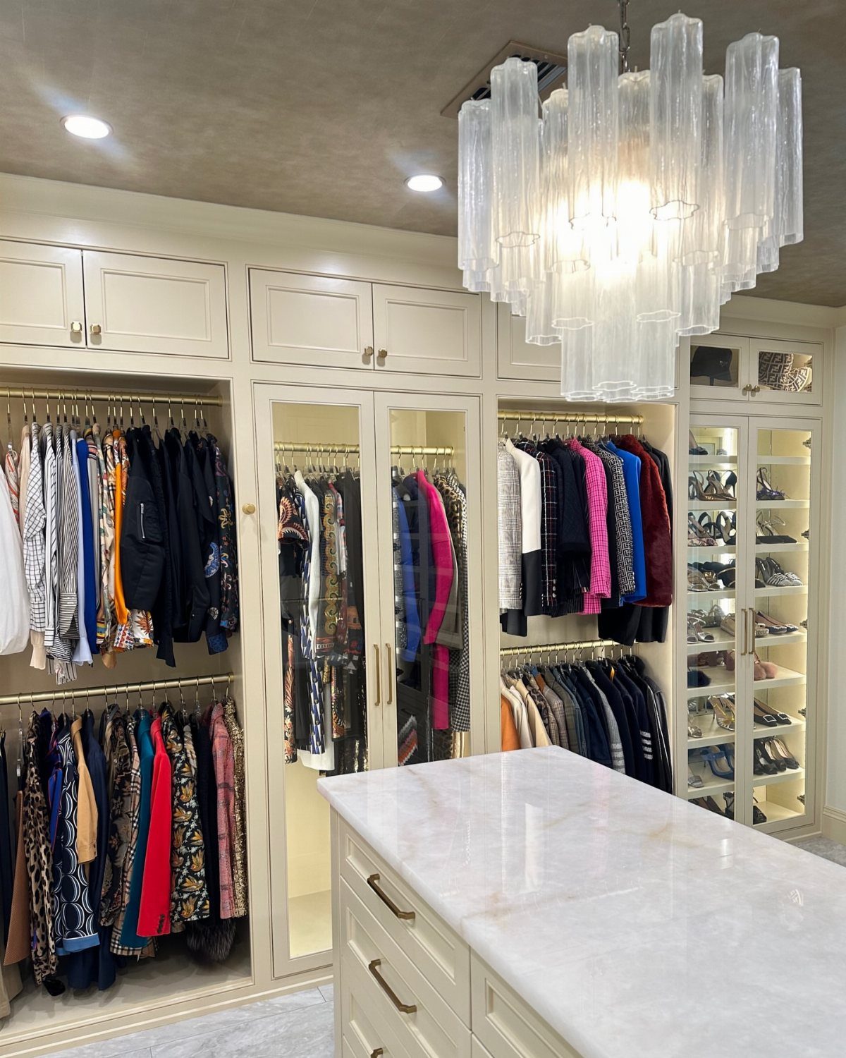 Luxury walk-in closet with white cabinets, marble island, and recessed ceiling lighting.