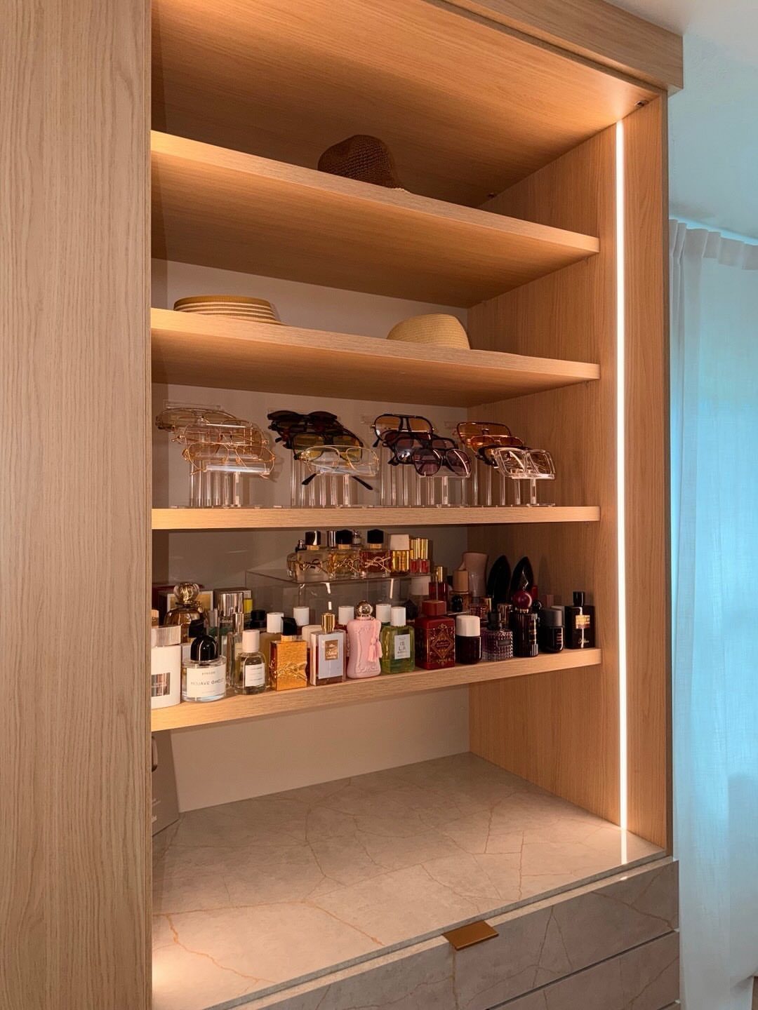 Wooden closet shelves with a vertical recessed LED light strip illuminating perfumes and accessories