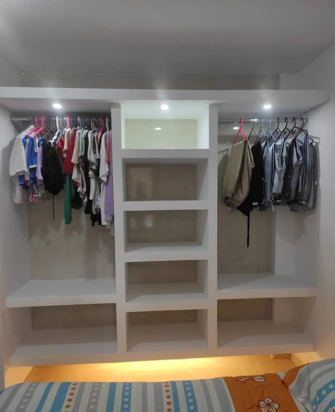 White built-in closet with recessed task lighting illuminating hanging clothes and shelves.