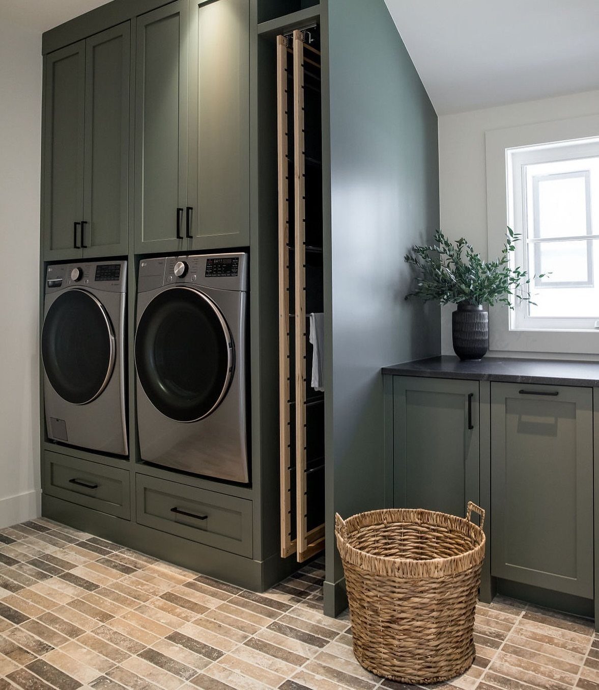 Pull-out wooden drying rack next to a washer and dryer in green cabinetry.