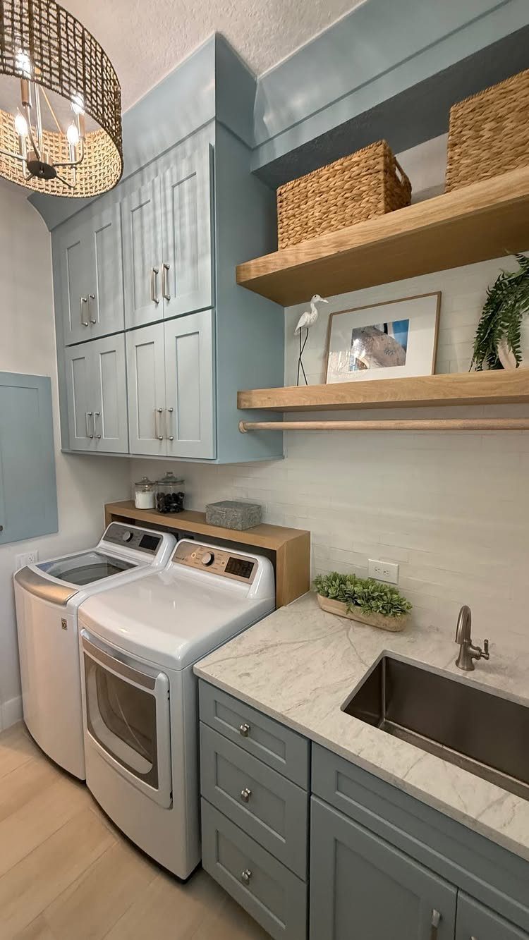 Light-wood floating shelves with baskets above white washer and dryer in blue laundry room