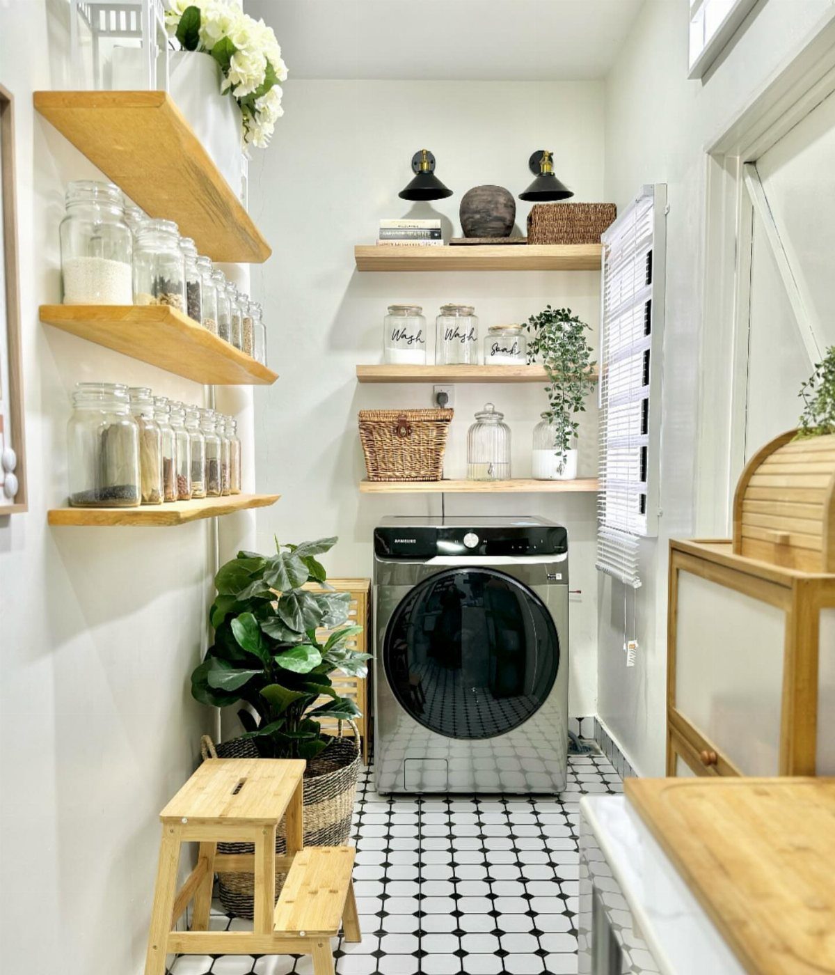 Glass jars and baskets on wooden floating shelves above a silver washing machine.