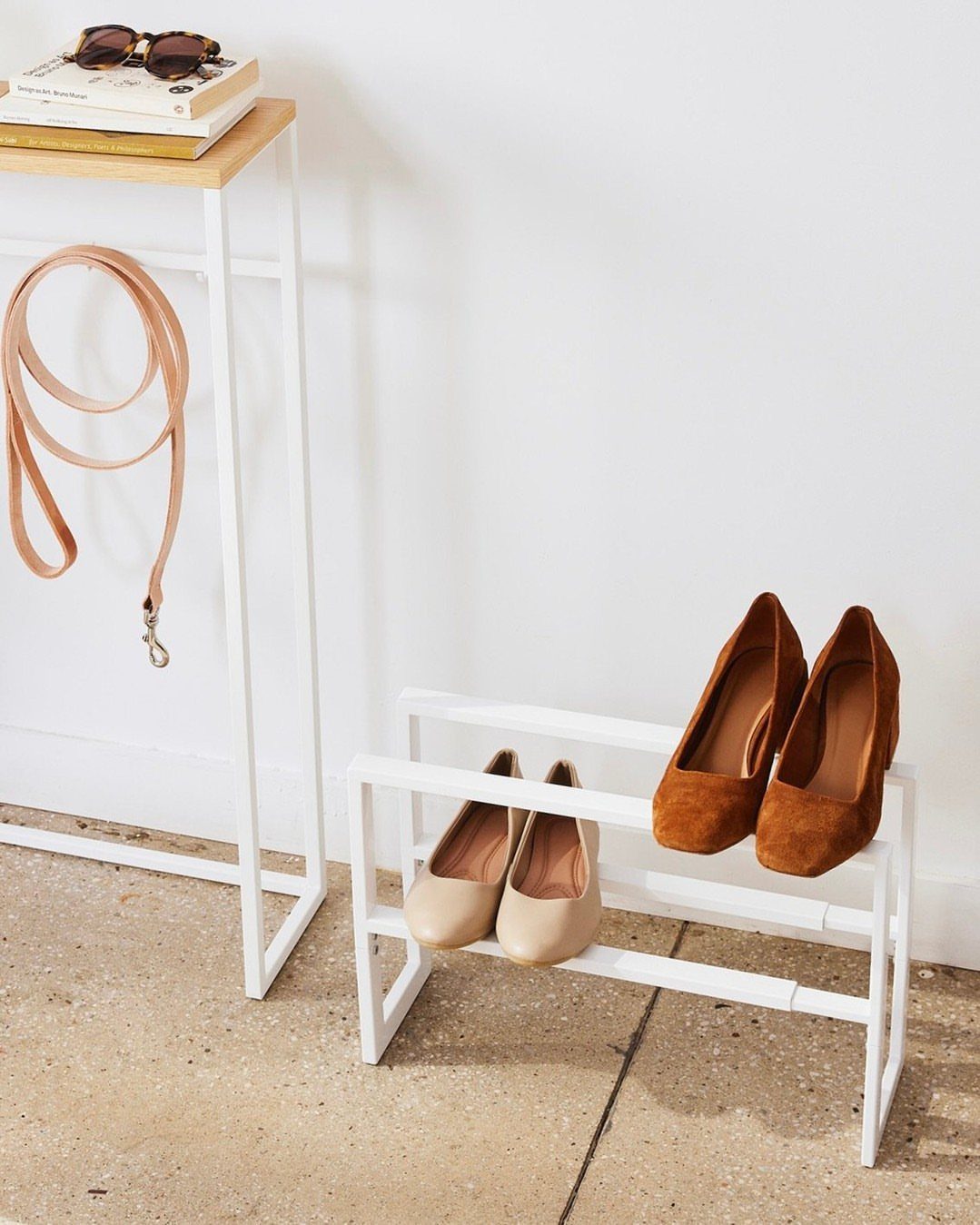 White metal shoe rack holding beige and brown flats next to a console table.