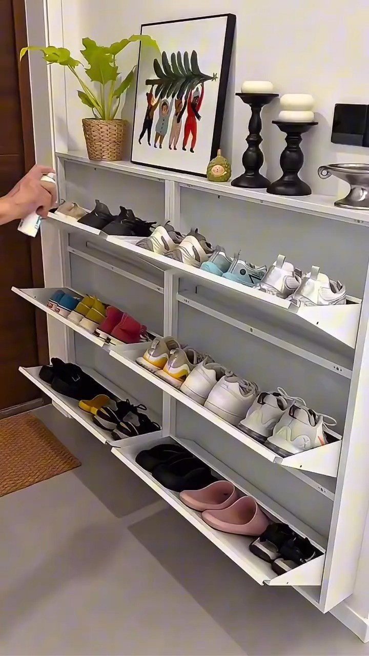 White tilt-out shoe cabinet with open drawers displaying various sneakers in a room.