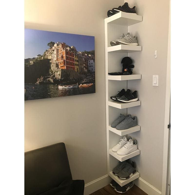 White vertical corner shoe shelf holding various sneakers in a room corner.