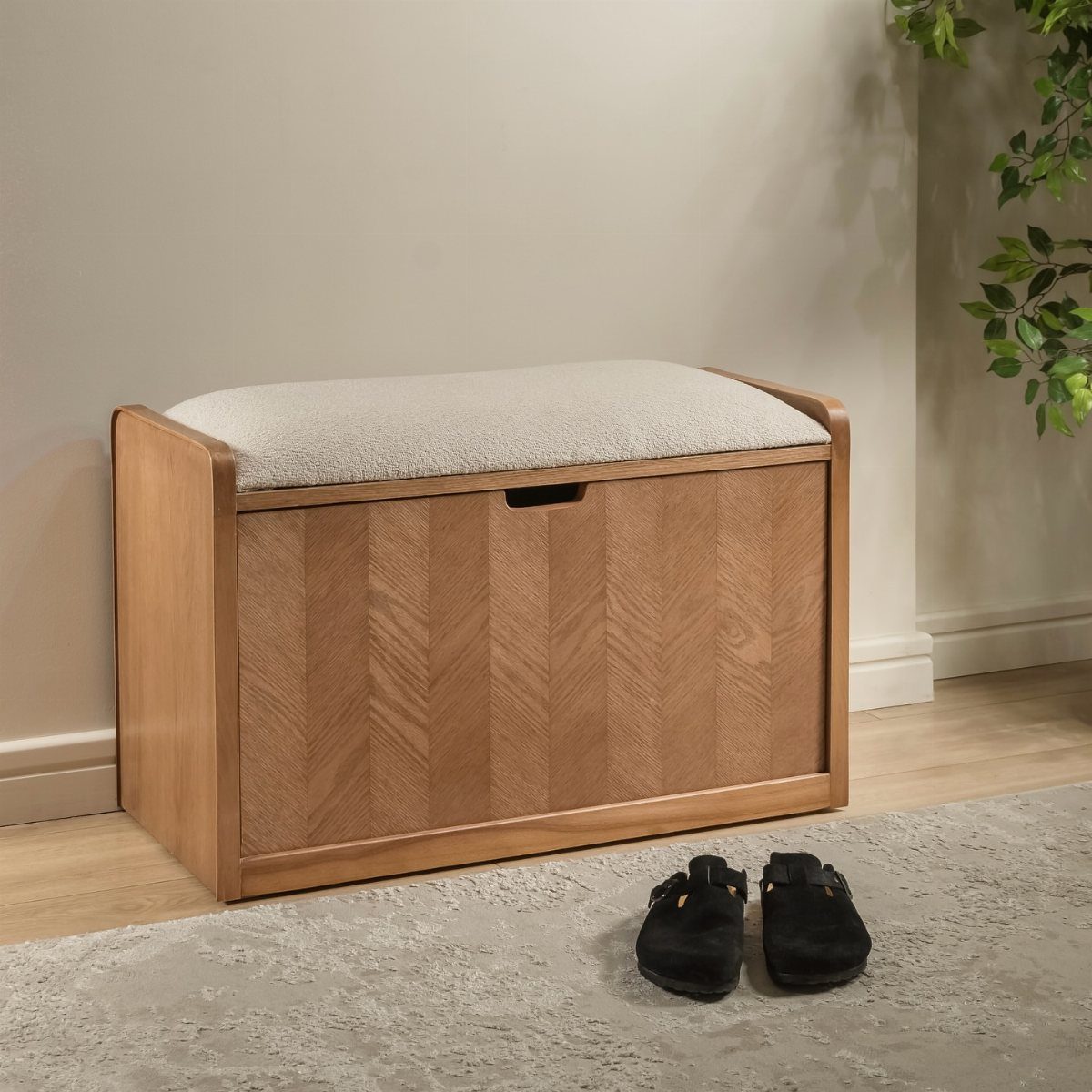Wooden storage bench with white cushion and black shoes on a grey rug