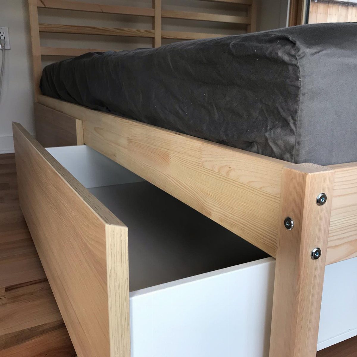 Wooden bed frame with a large open under-bed storage drawer on wooden flooring