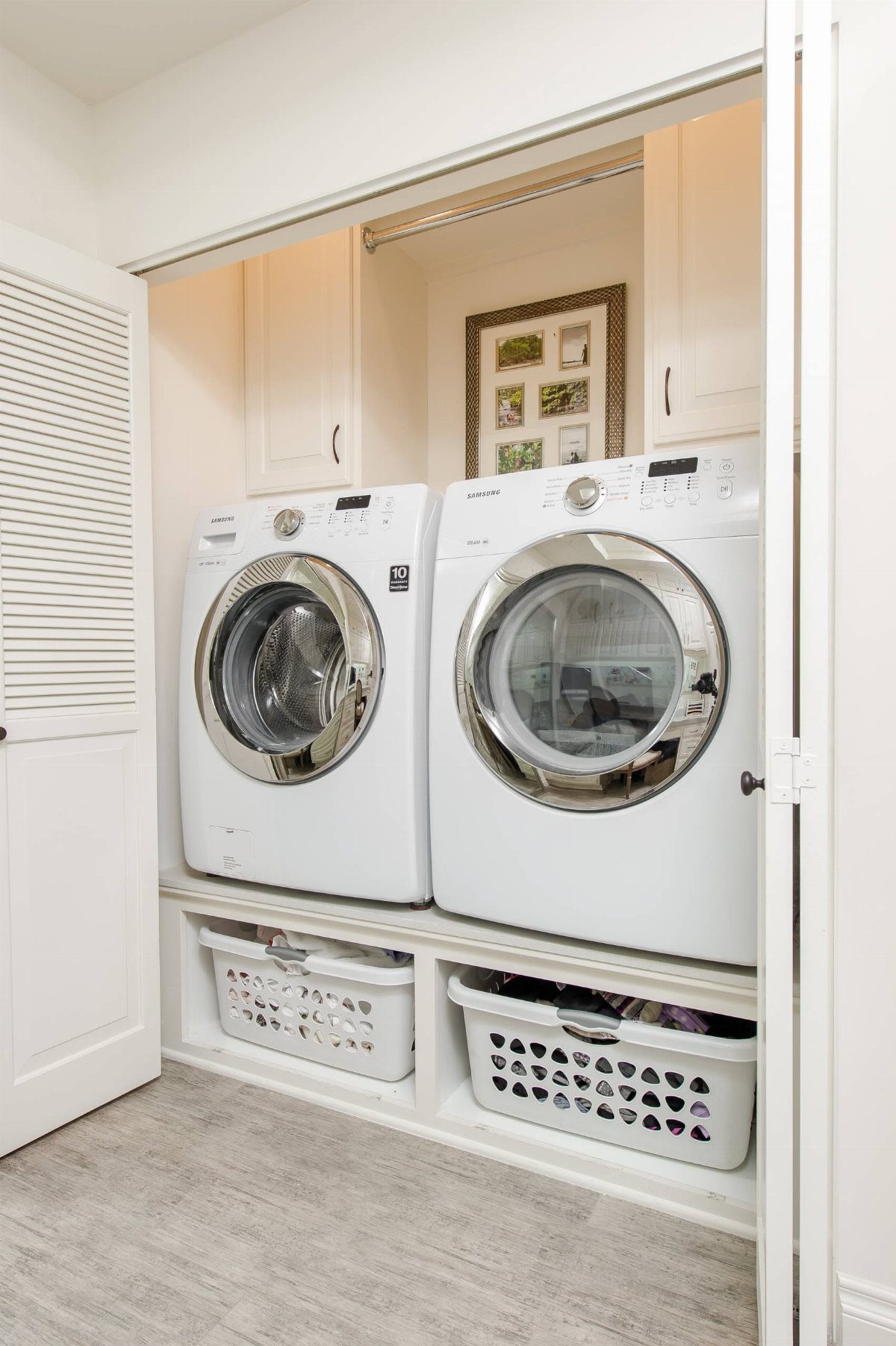 White side by side washer and dryer in a laundry closet with baskets below.