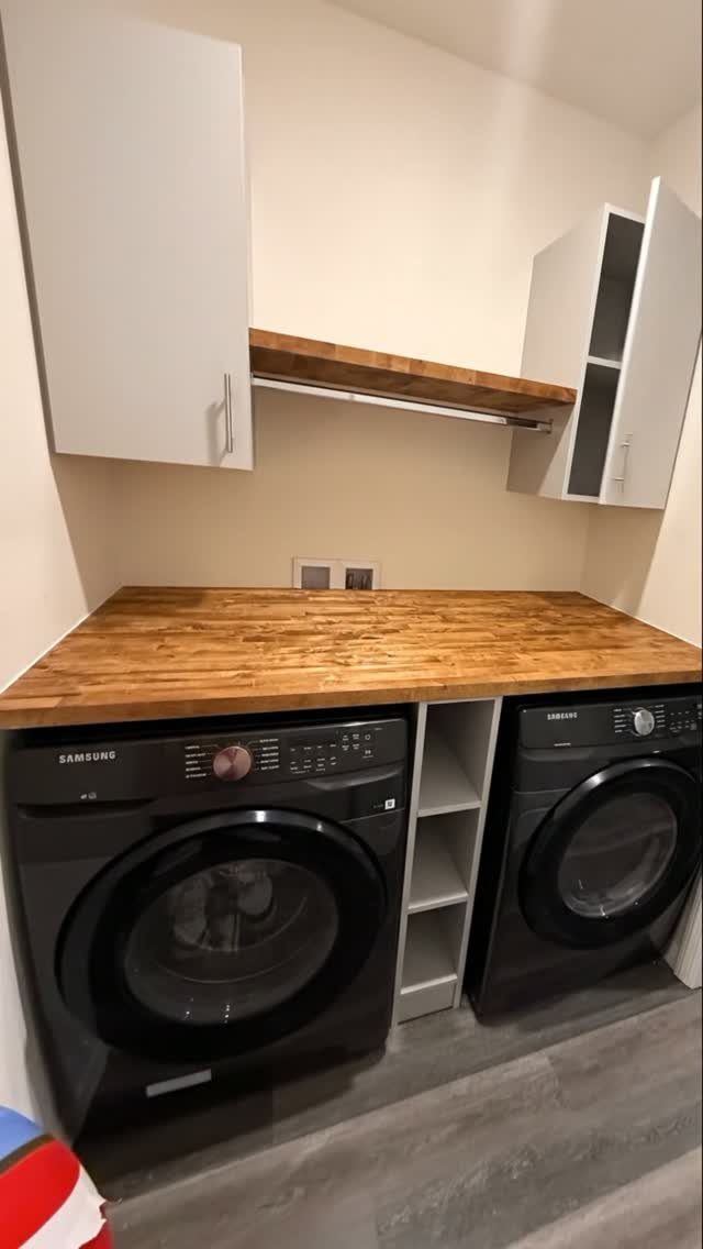 Two black front-load laundry machines installed side by side under a wooden countertop.