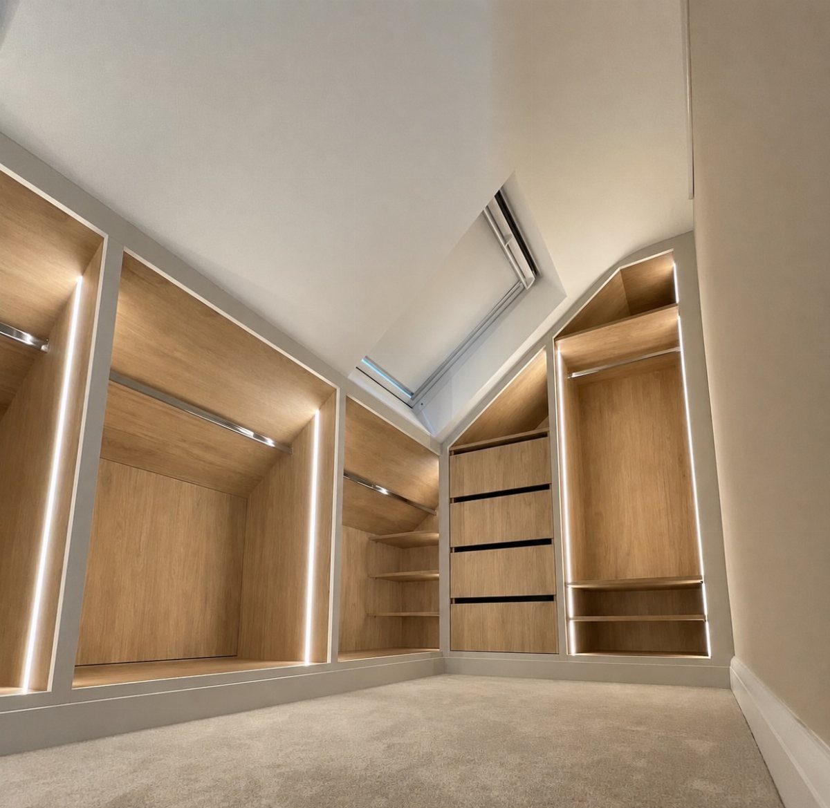 Custom light-wood shelving and drawers built into a slanted roof closet with LED lighting.