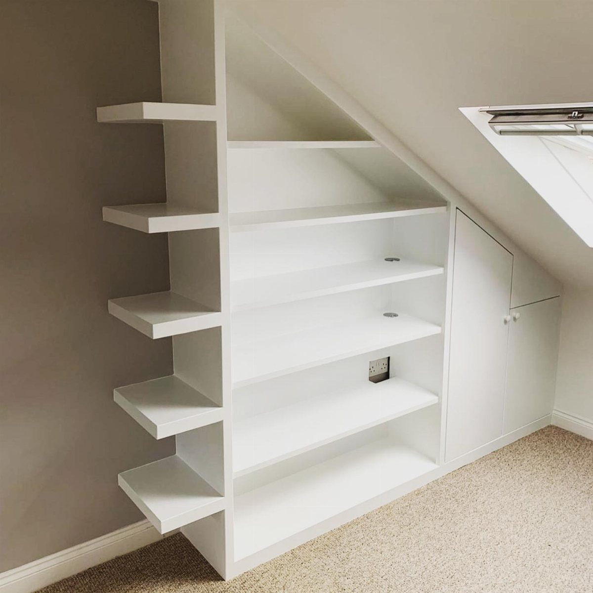 White built-in graduated shelves following the angle of a slanted attic ceiling.