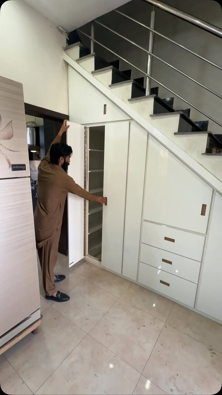 White built-in closet with a slanted top installed under a staircase with metal railings.