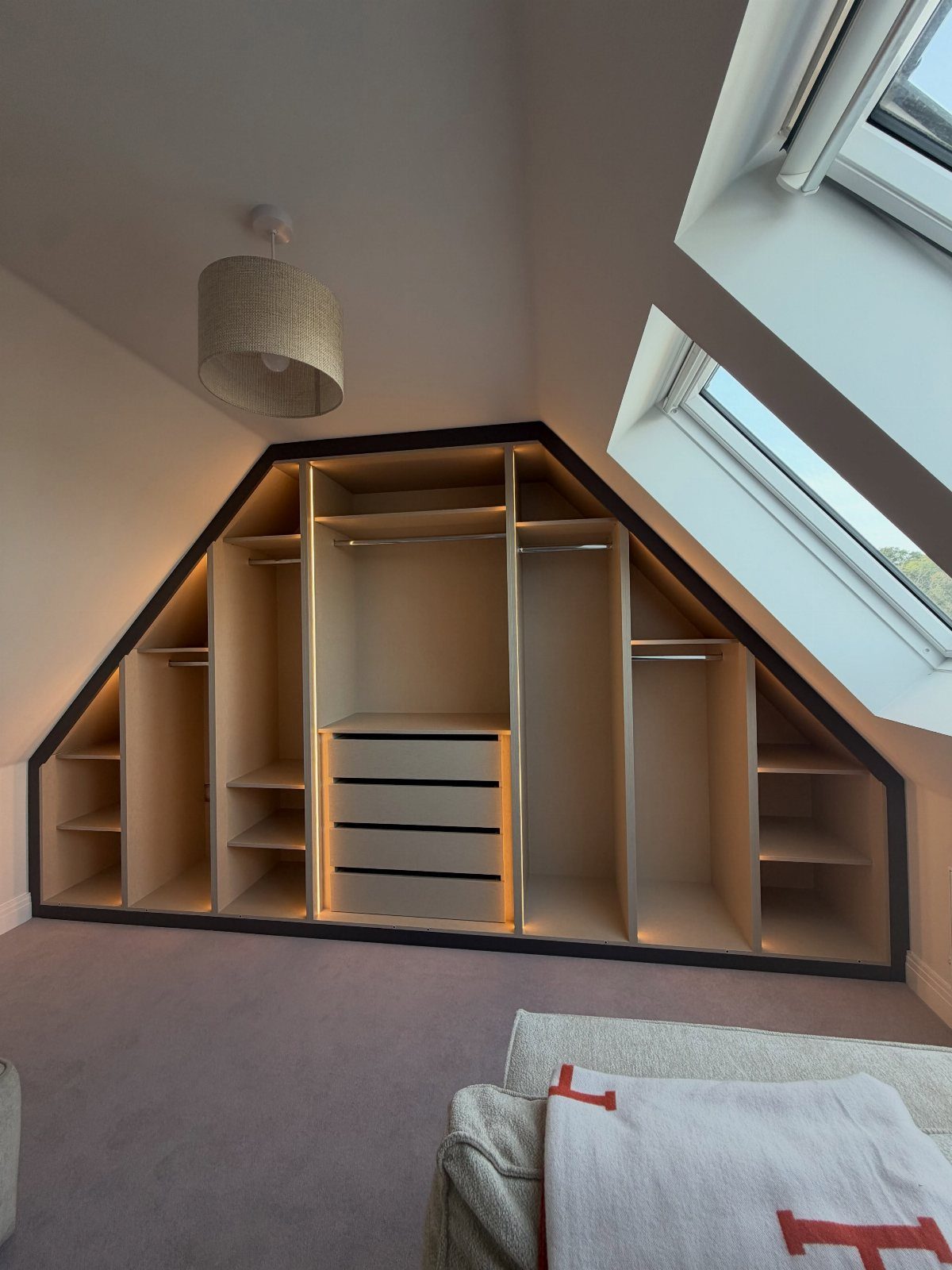 Custom built-in closet with integrated lighting fitted under a sloped bedroom ceiling