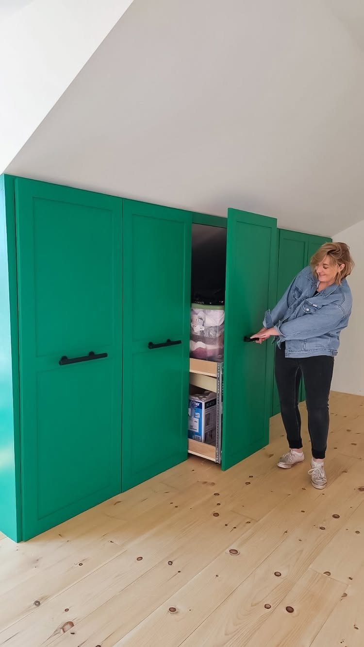 Green built-in closet under a sloped ceiling with a woman opening a door.