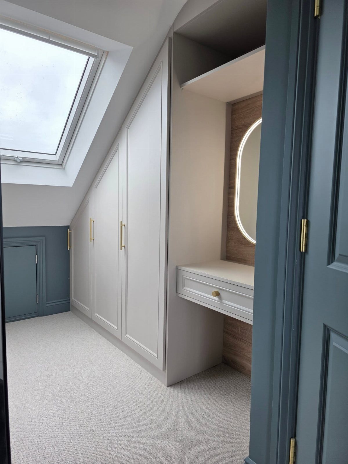 White built-in wardrobes and a vanity desk under a sloped ceiling with skylight.