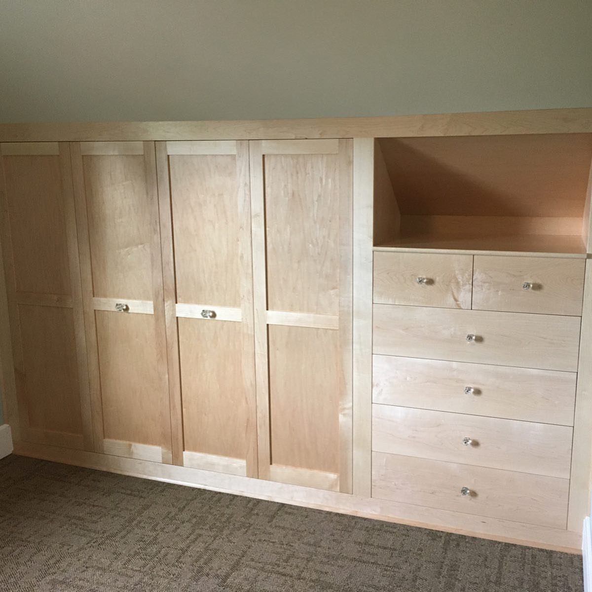 Light wood built-in cabinets with deep drawers under a sloped ceiling