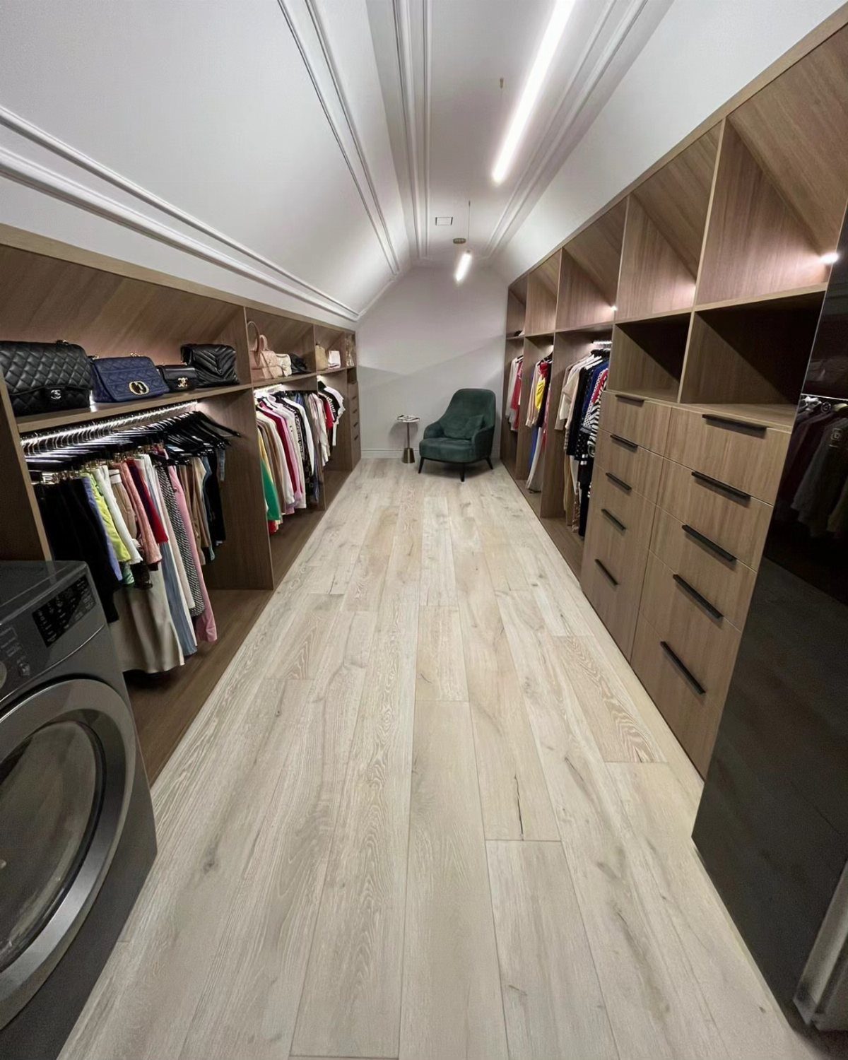 Walk-in closet with light wood shelving and hanging clothes under a sloped ceiling.