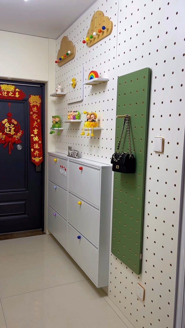 White narrow shoe storage cabinet with colorful knobs against a white pegboard wall.