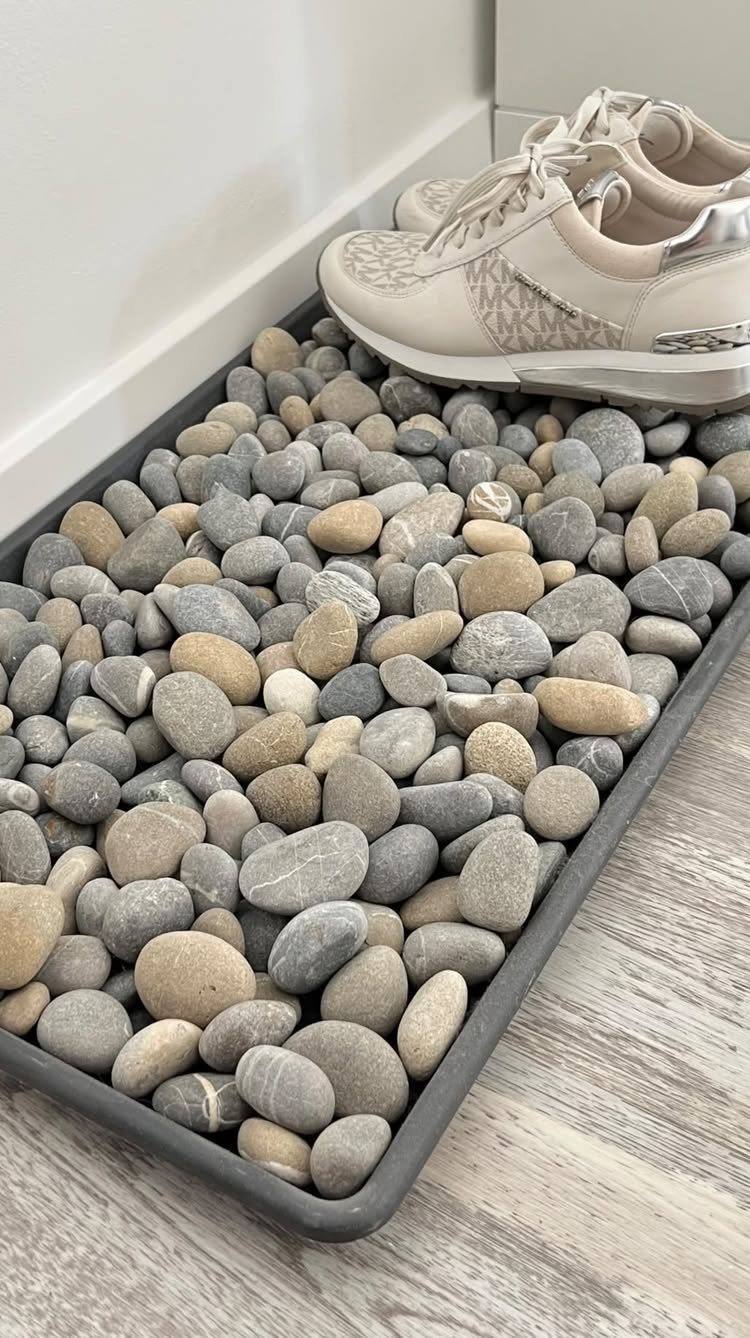 Beige sneakers resting on a stone-filled grey tray in a small entryway.
