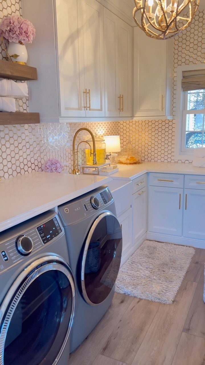 Laundry room with white cabinets, gold accents, and pink flowers on open shelving.