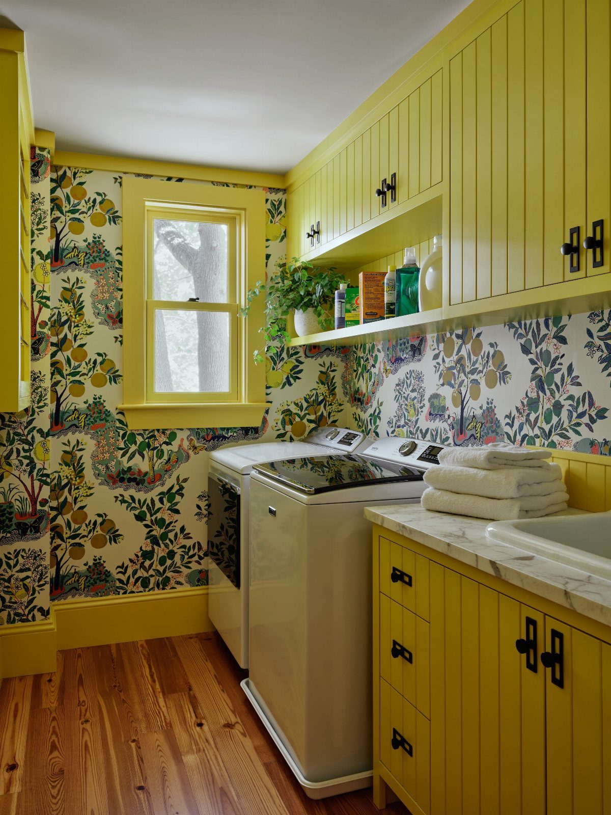 Bright yellow laundry room cabinets and botanical wallpaper surrounding a white washer and dryer.