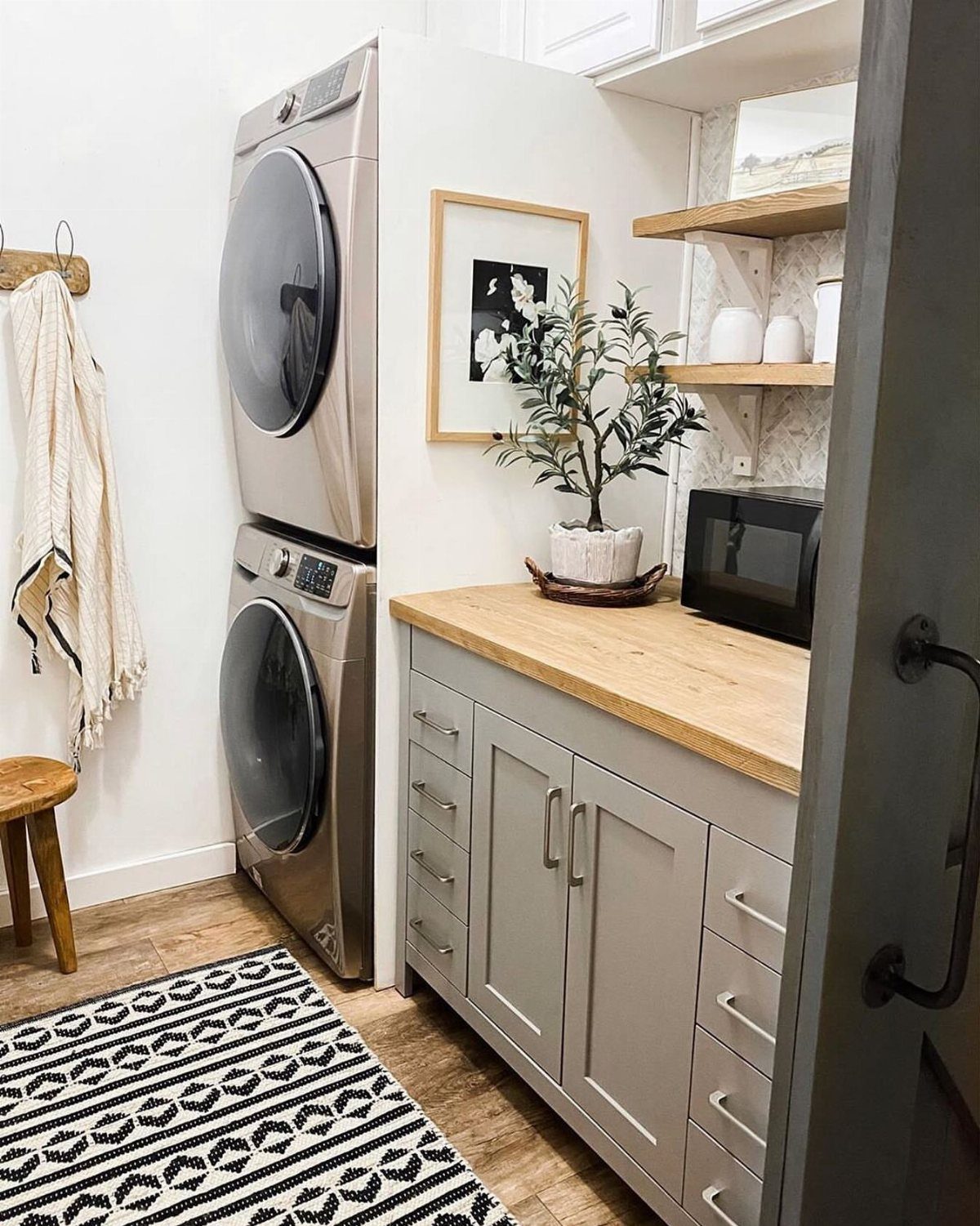 Stacked silver washer and dryer next to grey cabinets with a wood countertop.