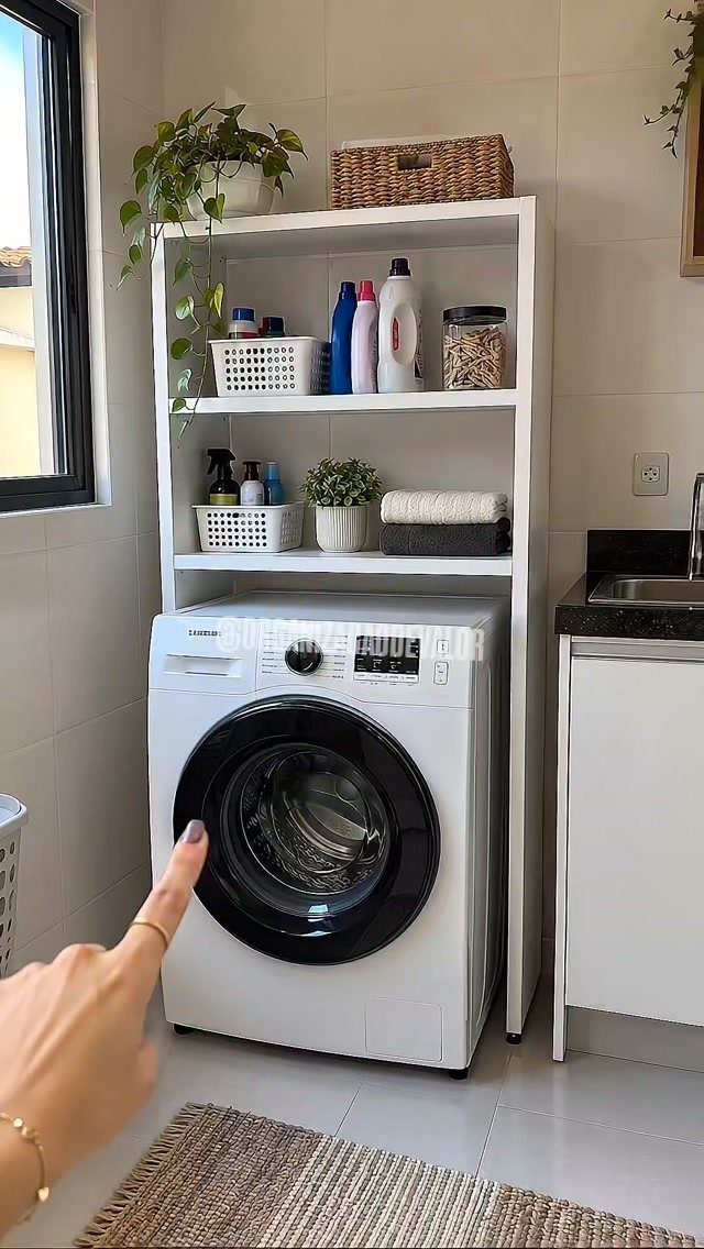 White washing machine under a white shelving unit with laundry supplies and plants.